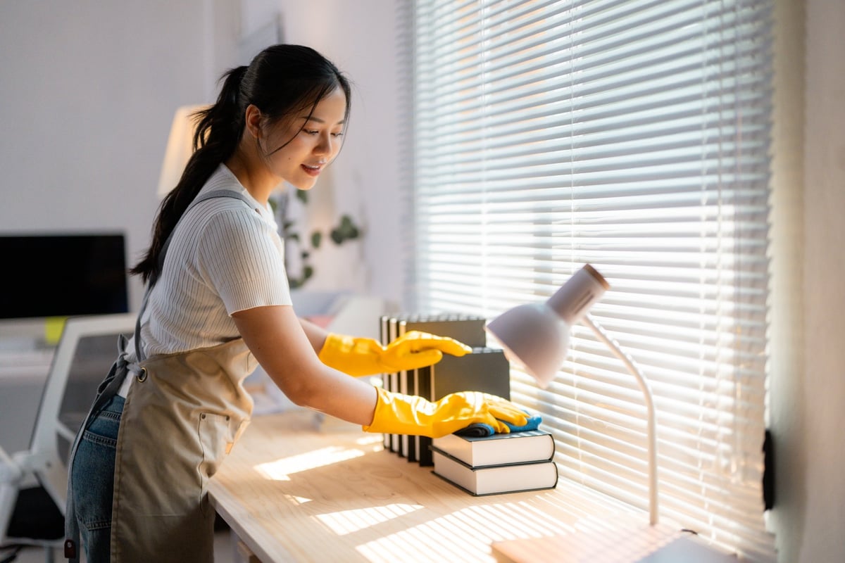 Yellow-gloved woman sanitizing books, organizing desk space in home office