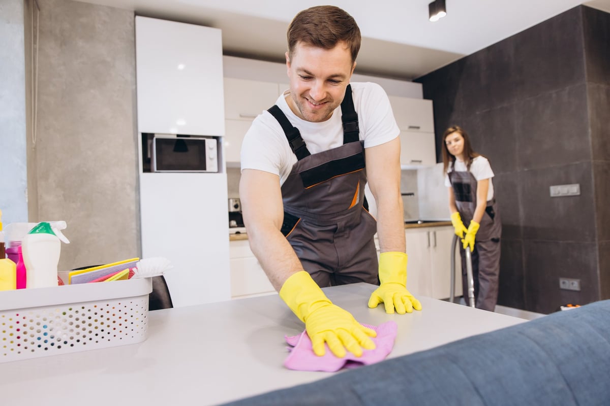 Cleaning company employees wearing uniforms and yellow gloves cleaning a kitchen